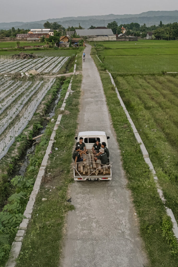 This image shows staff from Nusantara Lifestyle riding in the bed of a white pickup truck with a load of reclaimed teak wood that will be used to make sustainable furniture.