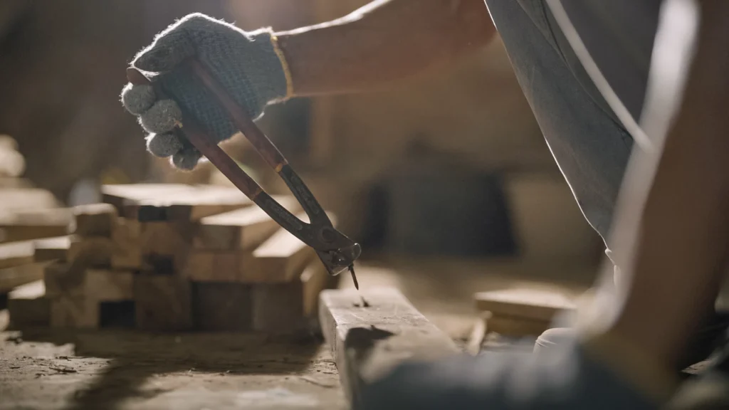 Close-up of hands removing old nails from reclaimed teak wood using pliers.