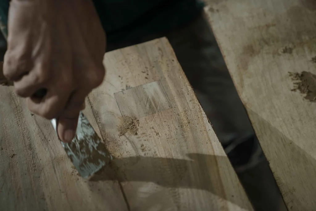 Craftsman filling small cracks and holes in reclaimed teak wood to prepare it for furniture construction.