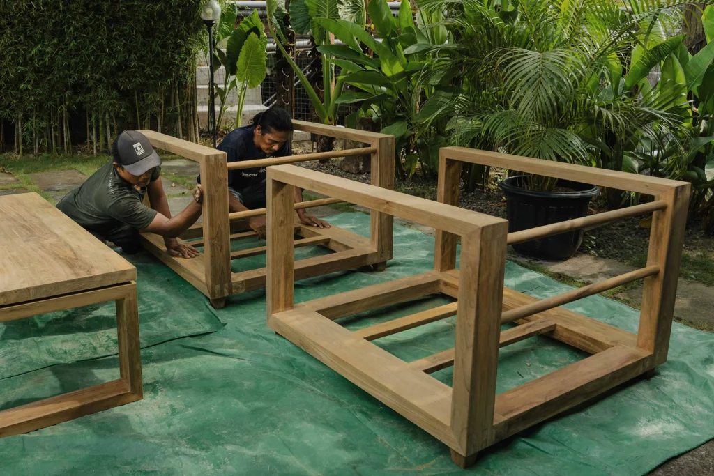 Craftsmen sanding reclaimed teak and applying an eco-friendly finish to bring out the natural grain of the wood.