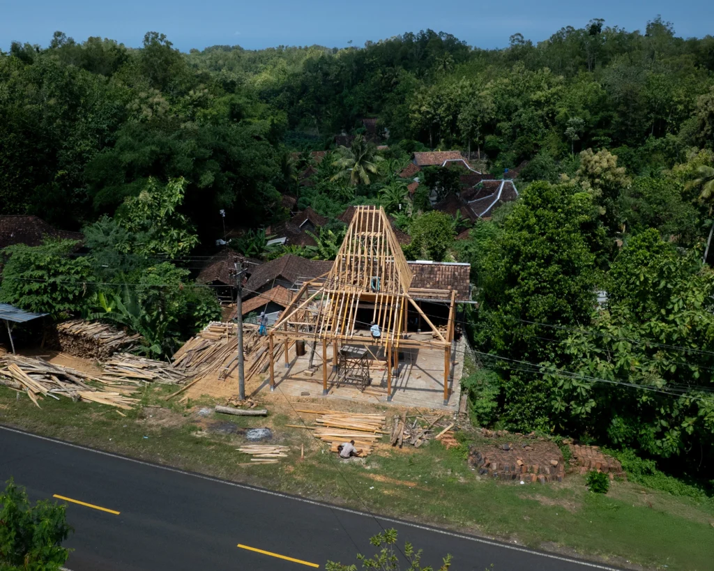 A group of men and women assembling a joglo frame in a rural Javanese village, illustrating the tradition of gotong royong.