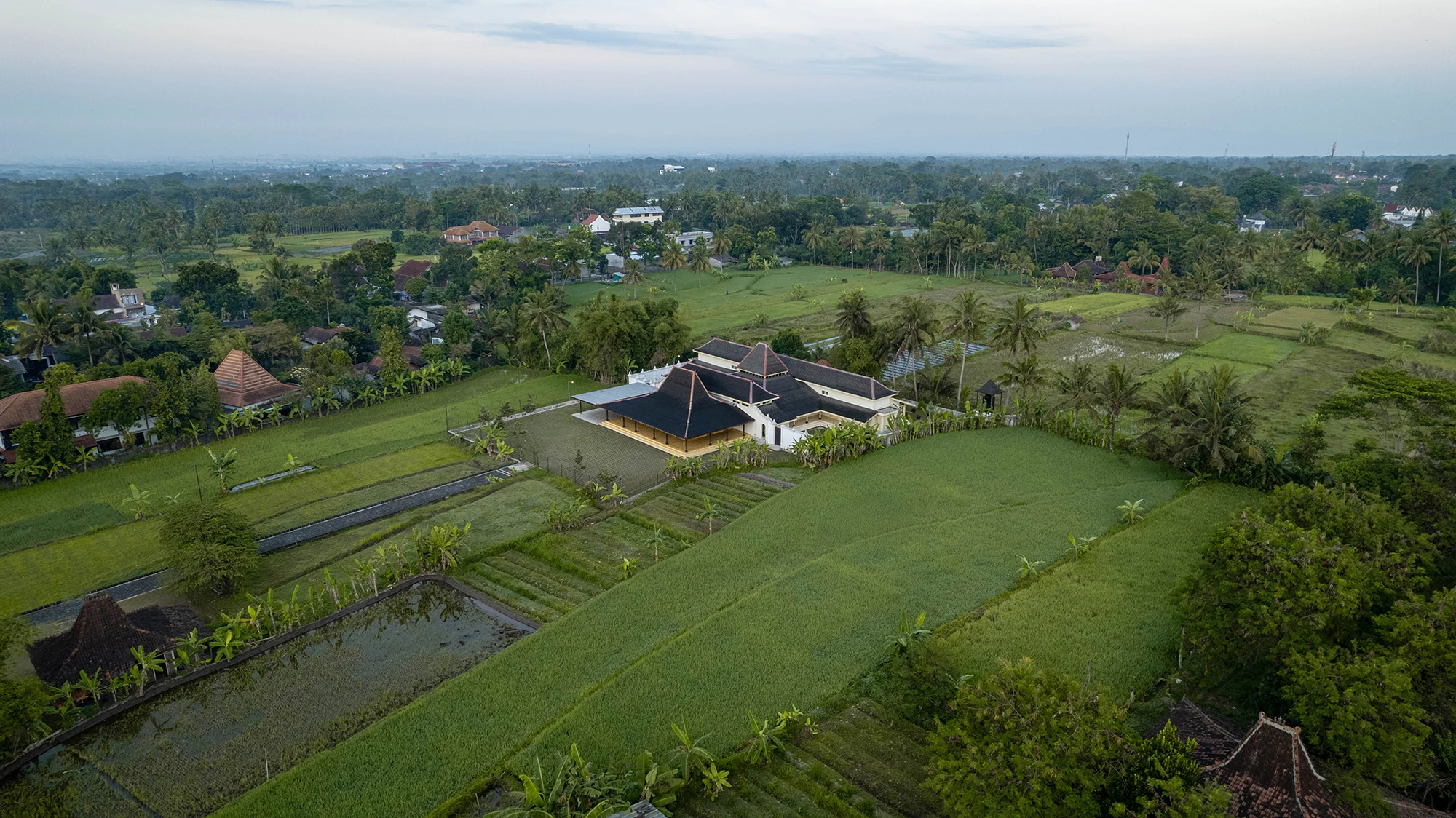 A well-preserved Javanese joglo house with its distinctive tiered roof, surrounded by lush greenery in Central Java.