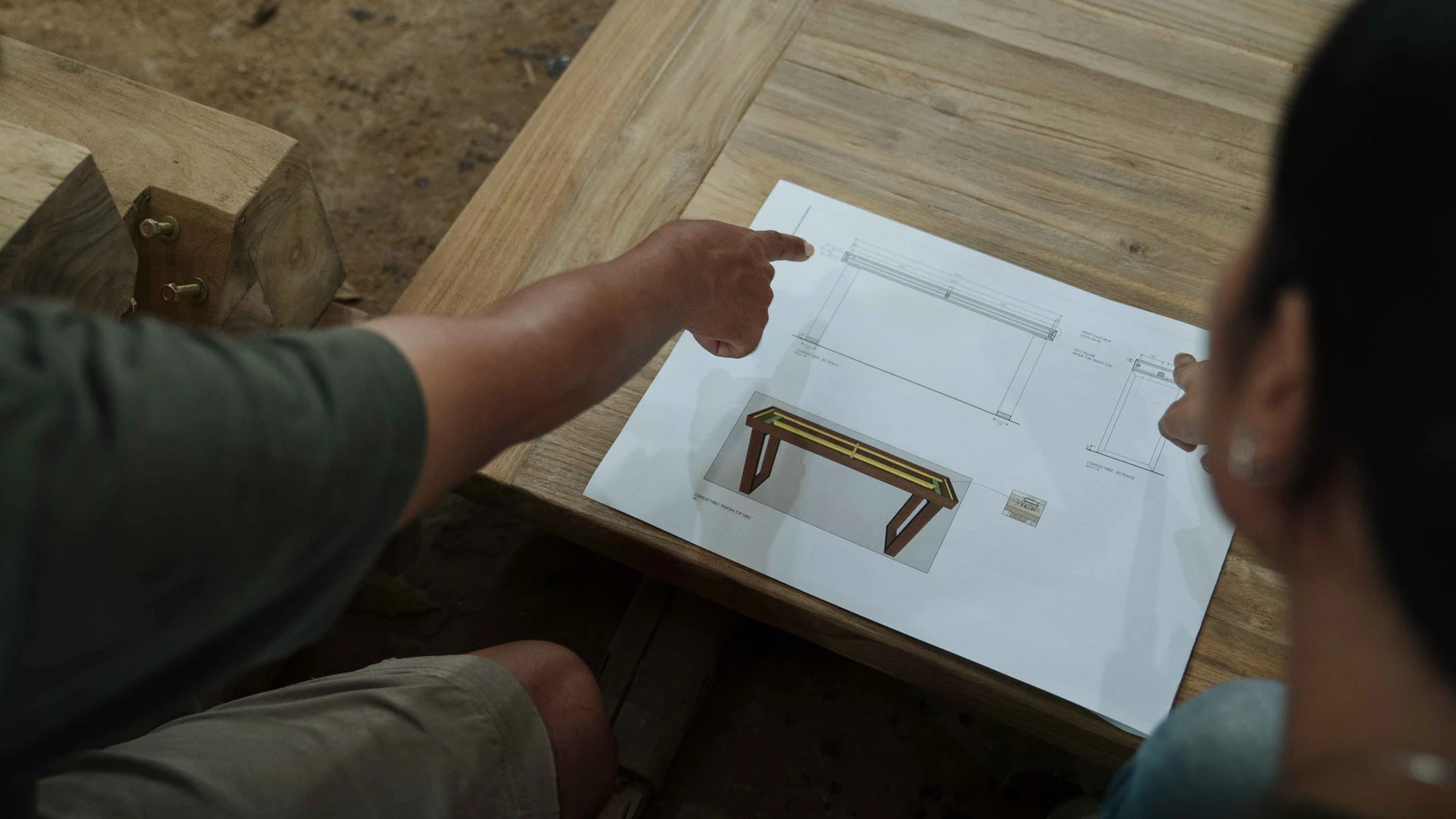Two people collaborate on the design development stage by reviewing technical project drawings for custom furniture.