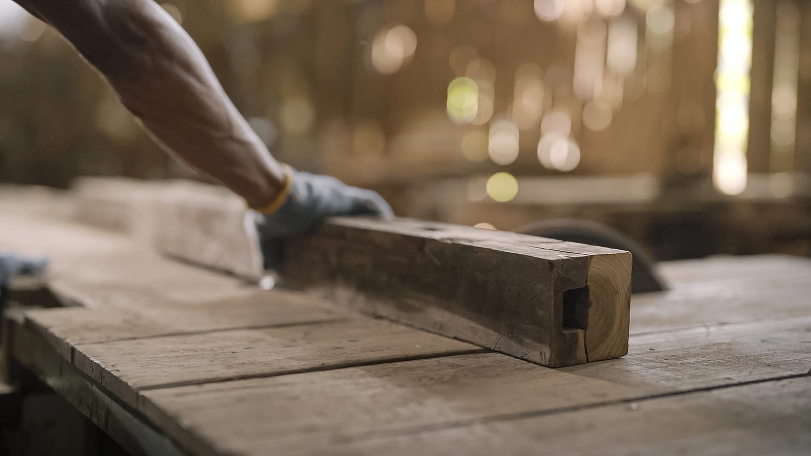 Indonesian artisan handling a reclaimed teak beam for Nusantara Lifestyle's sustainable woodworking process.