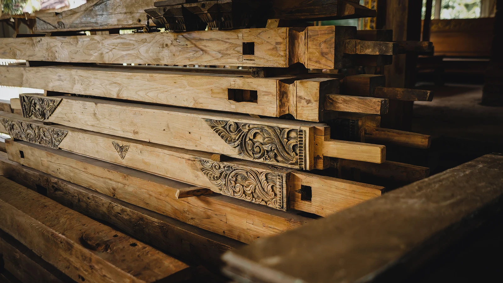 Salvaged reclaimed teak beams with traditional Javanese carvings from an old joglo, repurposed by Nusantara Lifestyle into sustainable furniture.