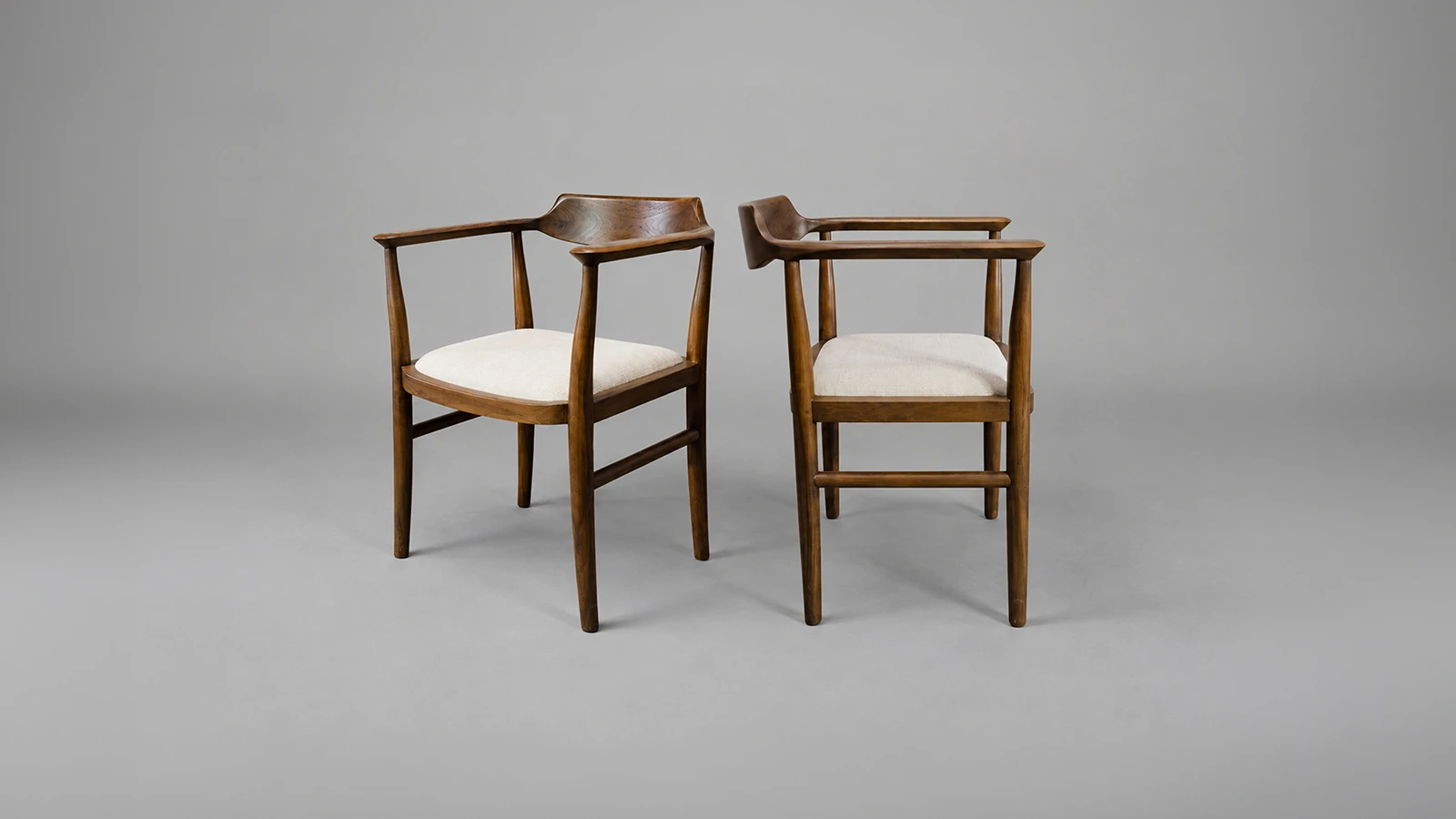 Two contemporary reclaimed teak dining chairs by Nusantara Lifestyle, featuring sculpted wooden backrests, curved armrests and natural upholstered seats.